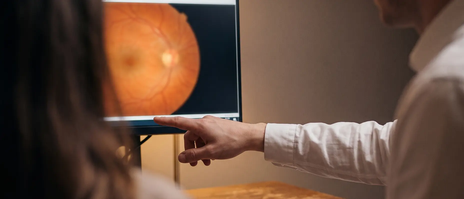 Two people at a desk, one pointing at a retinal image on the screen